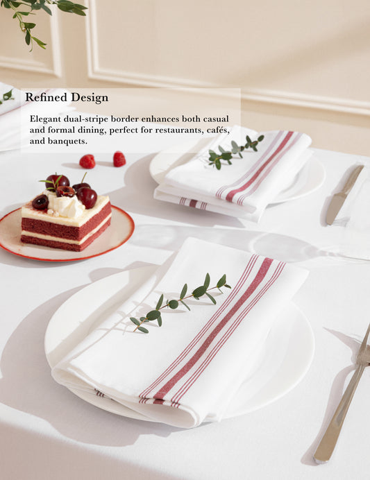 White tablecloth with red stripe cloth napkin, set on a dining table with a cake and silverware.